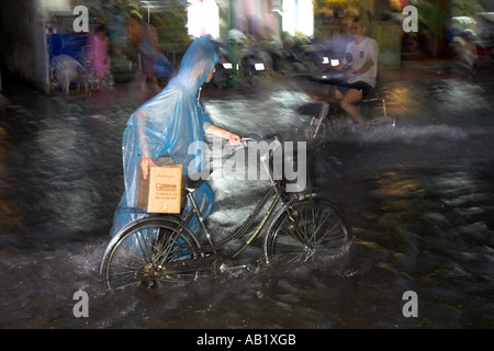 Ciclista in plastica cape spinge in bicicletta lungo allagato De Tham Street Pham Ngu Lao district Ho Chi Minh City Vietnam Foto Stock