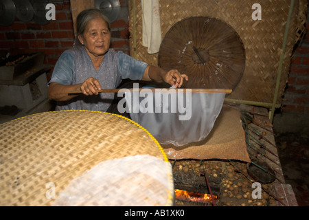 Anziani wooman rendendo la carta di riso sul panno riscaldato e cesto tessuto forma delta del Mekong Vietnam Foto Stock