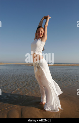 Giovane donna sorridente sulla spiaggia con i bracci sollevati Foto Stock