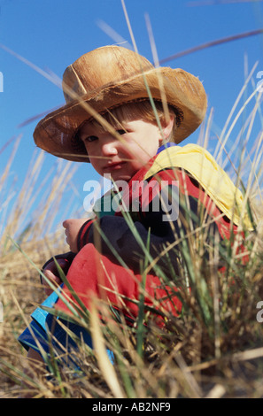 Un piccolo ragazzo in un cappello da cowboy in seduta erba lunga Foto Stock