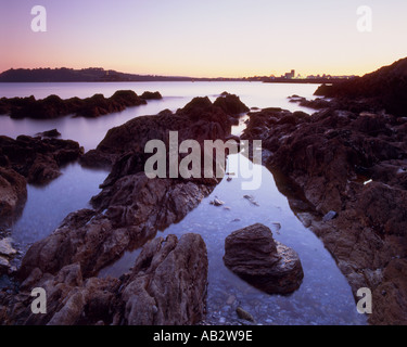 Mountbatten Bay Plymouth Devon al tramonto con il rock, la spiaggia e il mare di acqua in primo piano e bagliore arancione Foto Stock