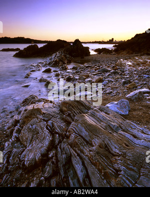 Mountbatten Bay Plymouth Devon al tramonto con il rock, la spiaggia e il mare di acqua in primo piano e bagliore arancione Foto Stock