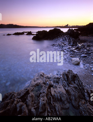 Mountbatten Bay Plymouth Devon al tramonto con il rock, la spiaggia e il mare di acqua in primo piano e bagliore arancione Foto Stock