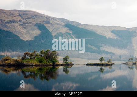 Alberi sulle isole riflessa nelle acque ancora di Loch Leven Ballachulish Glencoe Highlands della Scozia Foto Stock