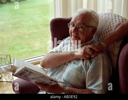 Il vecchio uomo lettura mentre tenendo la sua moglie s mano Foto Stock