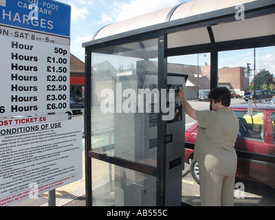 Donna matura automobilista che paga con le monete nel parcheggio auto, cabina coperta presso un ente locale paga a piedi 2003 cartello parcheggio Essex England UK Foto Stock