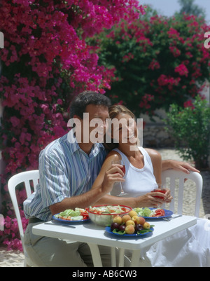 Coppia giovane bere e mangiare al fresco sulla terrazza con bougainvillaea fiori in background Foto Stock