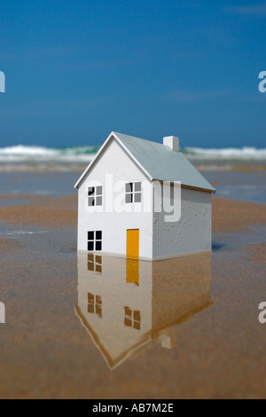 Modello di casa di affondare nella sabbia con le onde del mare in background Foto Stock