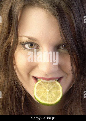 Ritratto di un giovane i capelli castani donna con Limetta dolce fetta nella sua bocca, Germania Foto Stock