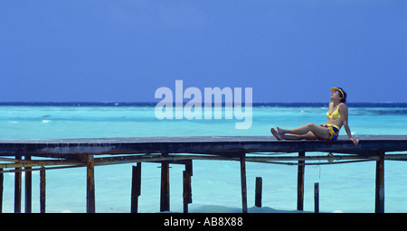 Giovane donna su un pontile, bagni di sole, Maldive. Foto Stock