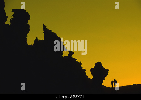 Due persone di fronte stranamente modellate rocce, sagome all'alba, Oman. Foto Stock