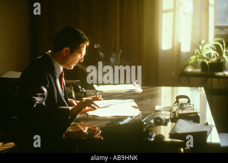 Imprenditore italiano di fumare al banco nel tardo pomeriggio la luce del sole ufficio finestra lavoratore executive fumatori fumo desk organizza organizzare Foto Stock