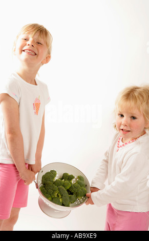 Ragazza giovane e un bambino con un colino di cime di broccoli Promozione di mangiare le verdure come parte di una sana dieta bilanciata Foto Stock