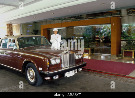 Porter si estende wai saluto al fianco di Rolls Royce Silver Shadow fuori Grand Hyatt Hotel ingresso, fattorino in blu visibile dietro, Bangkok, Thailandia Foto Stock