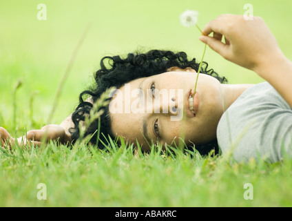Giovane donna sdraiata su erba con stelo di tarassaco in bocca Foto Stock