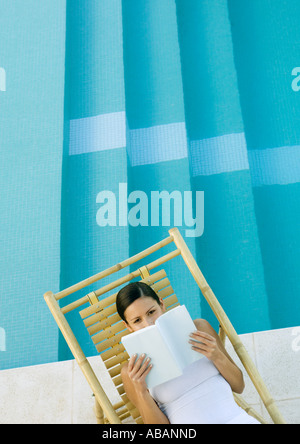 Donna lettura in poltrona accanto alla piscina Foto Stock