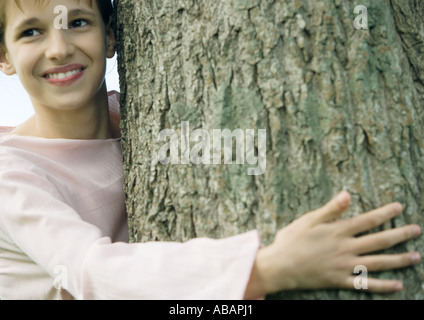 Ragazza con braccio intorno al tree, sorridente Foto Stock