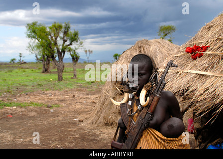 Donna del popolo Mursi indossando la decorazione di testa dei denti di animale Kalaschnikow e un bambino davanti al suo rifugio Etiopia Foto Stock