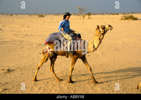 Trekking con il cammello giovane donna che indossa un cappello è a dorso di un cammello in sabbia in una vasta gamma di aprire il deserto di Thar vicino a Jaisalmer Rajasthan in India Foto Stock