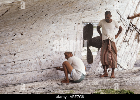 Un dhow's nakhoda, o comandante, impermeabilizzanti lo scafo del suo dhow dove necessario. Il sambuco, costruito in Sur, Oman, incluso un motore Foto Stock