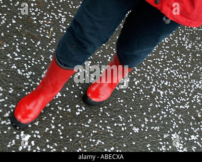 Le gambe di una persona della donna con red rubberboots andare a fare una passeggiata in condizioni di tempo piovoso su una strada con asfalto nero ricoperti in superficie Foto Stock