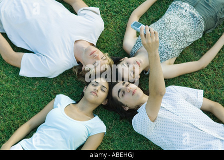 Un gruppo di giovani amici sdraiati sull'erba con teste insieme a occhi chiusi un prendere foto con il telefono cellulare Foto Stock