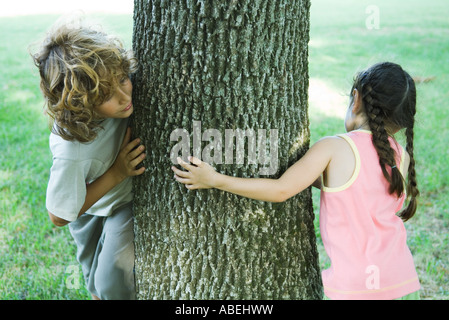 Ragazzo e una ragazza in piedi su entrambi i lati del tronco di albero, spiata intorno Foto Stock
