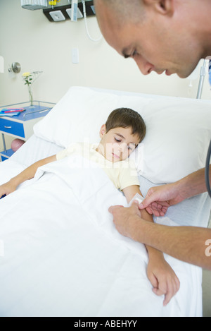 Ragazzo che giace nel letto di ospedale mentre il medico mette cerotto sul ragazzo del braccio Foto Stock