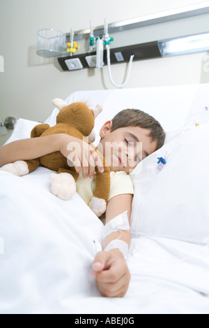 Bambino addormentato nel letto di ospedale dormendo, tenendo animali impagliati, sorridente Foto Stock