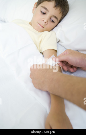 Ragazzo che giace nel letto di ospedale a guardare l'uomo messo benda tubo IV Foto Stock