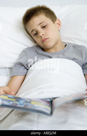 Ragazzo malato che giace nel letto di lettura del libro di fumetti Foto Stock