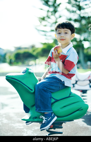 Ragazzo su attrezzature per parchi giochi, sorridente alla fotocamera, azienda apple Foto Stock