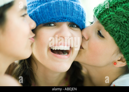 Giovani femmine baciato sulle guance da due amici, sorridente in telecamera Foto Stock