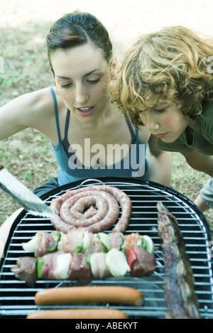 Giovane donna e ragazzo la piegatura su barbecue, guardando a grigliare carni Foto Stock