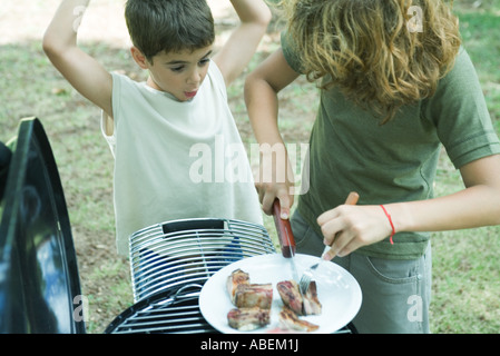 Ragazzo il taglio di carne sulla piastra mentre secondo boy orologi Foto Stock