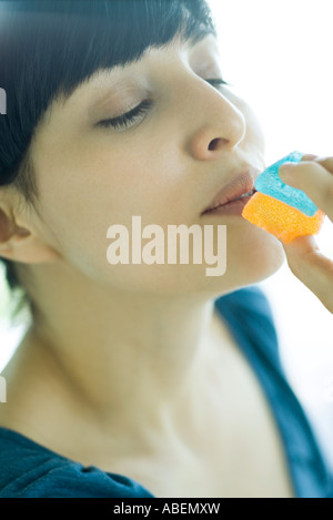 Donna che mantiene fino pezzo di caramella alla bocca, occhi semi-chiuso Foto Stock