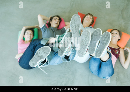 Quattro amici teen giacente sul dorso sul pavimento, tenendo su gambe, concentrarsi su suole di scarpe Foto Stock