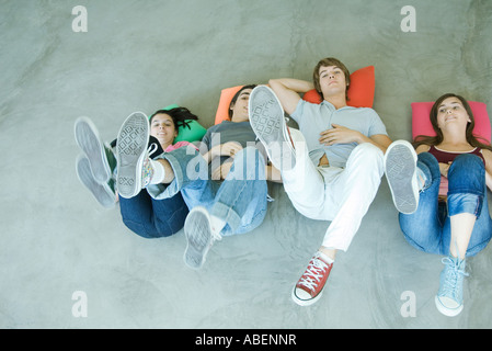 Quattro amici teen giacente sul dorso sul pavimento, tenendo su gambe, concentrarsi su suole di scarpe Foto Stock