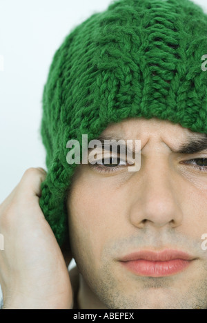 Giovane uomo che indossa knit hat, solcando brow, ritratto, close-up Foto Stock