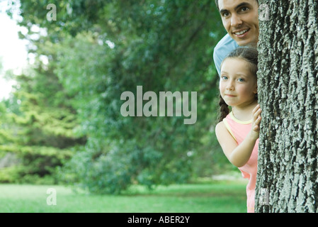 Ragazza e padre peeking intorno tree Foto Stock