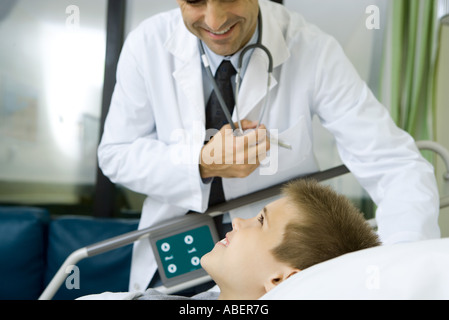 Bambino giacente in letto di ospedale, dottore in piedi a fianco Foto Stock