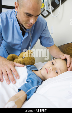 Ragazza distesa nel letto di ospedale, infermiere, la mano sulla fronte della bambina Foto Stock