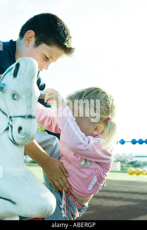 Ragazzo aiutando la ragazza su cavallo a dondolo Foto Stock