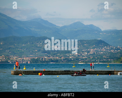 La gente sul molo e un uomo in acqua vicino a Peschiera del Garda Lago di Garda Italia un posto popolare per gli sport acquatici Foto Stock