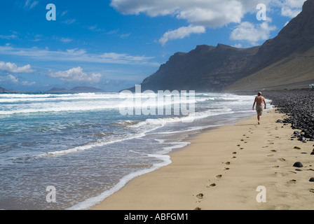 dh Playa de Famara FAMARA LANZAROTE turista a piedi lungo la spiaggia sabbiosa El Risco scogliere e baia passi la caleta spiagge Foto Stock