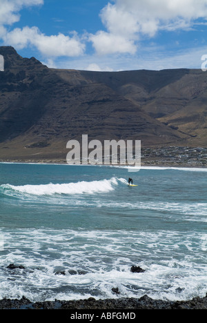 Dh Playa de Famara Lanzarote Lanzarote Surfer cavalcare le onde da surf El Risco de Famara scogliere sul mare e sulla baia di onda surf Foto Stock