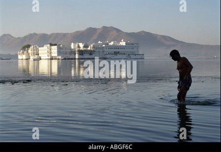 L'uomo prendendo un bagno nel lago Pichola con il Lago Palace Hotel in background, Udaipur Rajasthan (India) Foto Stock