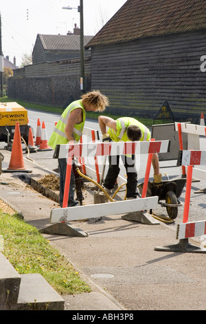 I lavoratori stradali lo scavo di una trincea di installare cavi in Stow Road in Ixworth, Suffolk, Regno Unito Foto Stock