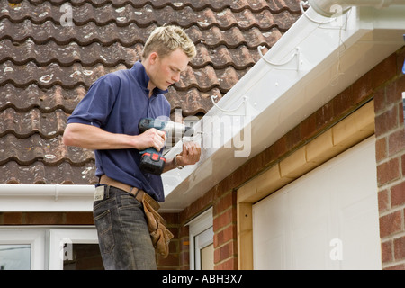 Un costruttore di installazione delle staffe per tenere una gronda al di sotto di un tetto di una casa. Foto Stock