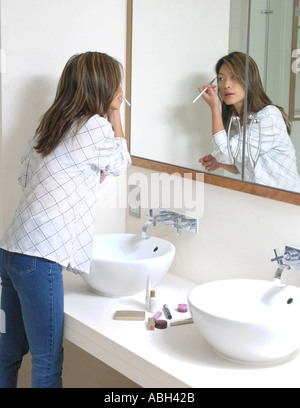 Giovane donna applicazione di realizzare in uno specchio in un elegante bagno bianco Foto Stock